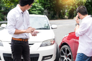 Accidente automovilístico con dos autos y conductores fuera de los vehículos.